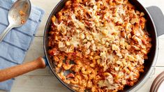 a casserole dish filled with pasta and cheese on a blue towel next to a wooden spoon