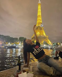 a woman sitting on the ground in front of the eiffel tower at night