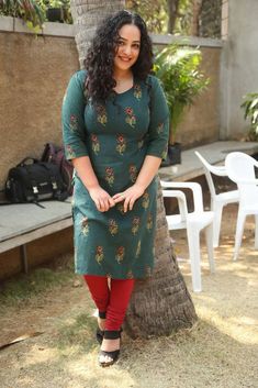 a woman standing in front of a tree wearing a green dress and red leggings