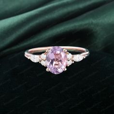 an engagement ring with a pink stone and white stones on it's sides, sitting on a green velvet background