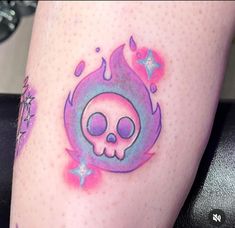 a colorful skull tattoo on the leg of a woman's legs with pink and blue ink