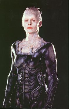 an alien woman with white hair and black skin is standing in front of a dark background