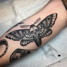 a black and white tattoo with a moth on it's arm, next to a skull