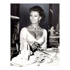 a woman sitting at a table in front of a wine glass and plate with utensils on it