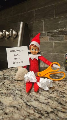 an elf holding a sign next to a pair of scissors on top of a counter