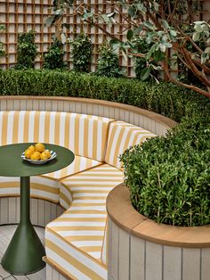 an outdoor seating area with yellow and white striped cushions, round tables and potted plants