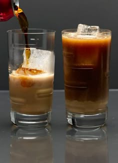 two glasses filled with liquid and ice on top of a gray table next to each other