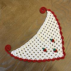 a crocheted triangle with red flowers on the bottom and white yarn around it