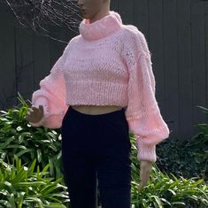 a mannequin wearing a pink sweater and black pants in front of some bushes