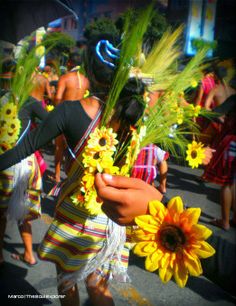 a group of people walking down a street with sunflowers on their heads and arms