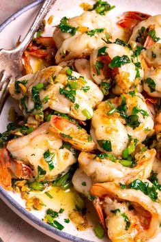 a white plate topped with shrimp covered in sauce and garnished with parsley