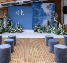 a stage set up for a wedding with flowers and greenery on the side, surrounded by stools