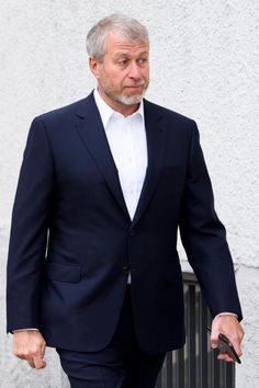 an older man in a suit walking down the street with his hand on his hip