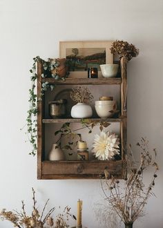 a wooden shelf filled with vases and flowers on top of a table next to candles