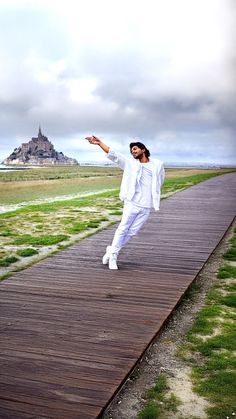 a man in white is walking on a wooden walkway with his arms out to the side