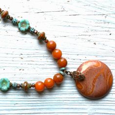 "18\"   Agate necklace made w/rustic red orange Jasper gemstone pendant,  8 mm Carnelian colored Agate beads, 4 mm Carnelian colored agate beads, 12 mm aqua & rustic red Lampwork accent beads, 8 mm accent Picasso glass beads, patina turquoise Bali style accent beads, 10 mm green Picasso flower glass accent beads, 6 mm caramel Picasso beads w/aqua finish, 3 mm patina turquoise disc spacers, 3 mm Picasso glass beads, antique brass bead caps, brass spacer beads and brass lobster claw clasp." Bohemian Orange Agate Jewelry, Orange Carnelian Bohemian Jewelry, Handmade Turquoise Agate Necklace For Healing, Bohemian Carnelian Jewelry In Orange, Bohemian Carnelian Orange Jewelry, Handmade Turquoise Agate Necklace, Artisan Jasper Beaded Necklaces As Gifts, Bohemian Agate Round Pendant Necklace, Orange Gemstone Bohemian Beaded Necklace