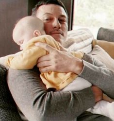 a man holding a baby in his arms while sitting on a couch next to pillows