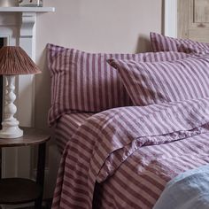 a bed with purple and white striped comforter next to a lamp on a table