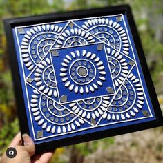 a hand holding up a blue and white tile with an intricate design in the middle