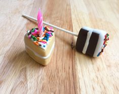 two cake pops with sprinkles and a birthday candle on them sitting on a wooden table