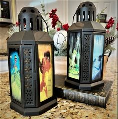 two black lanterns sitting on top of a table next to each other with pictures in them