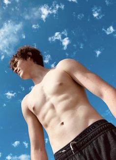 a man without a shirt standing in front of a blue sky