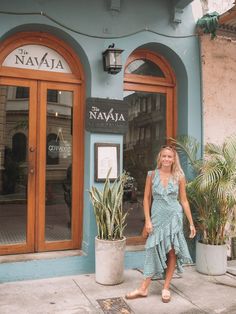 a woman standing in front of a blue building with potted plants on the sidewalk