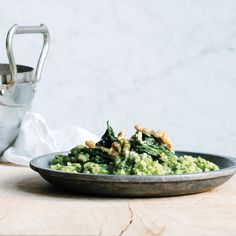 a bowl filled with broccoli and nuts on top of a wooden table next to a watering can