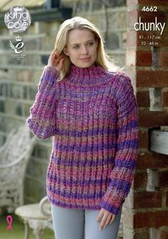 a woman wearing a purple and pink sweater standing in front of a brick wall with her hand on her head