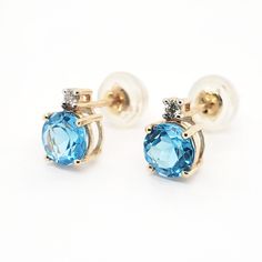 14k gold blue topaz and diamond gemstone earrings. Dainty matching pair of round blue topaz gemstones with 0.03ct H/vs diamonds set above in 14k solid gold. Blue Topaz gemstones are found in Brazil and Madagascar and is the birthstone for the month of November. The silicone push backs are secure and allow the stud to sit firmly on the earlobe. Blue Topaz Earring, Fine Jewelry Blue Topaz Round Earrings, Blue Round Diamond Earrings Fine Jewelry, Blue Diamond Round Earrings For Anniversary, Blue Topaz Earrings With Diamond Accents, Blue Topaz Birthstone Round Earrings, Blue Round Topaz Earrings, Blue Topaz Birthstone Earrings, Blue Fine Jewelry Earrings With Accent Stones