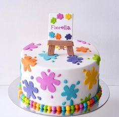 a white cake decorated with multicolored flowers and a wooden easel on top