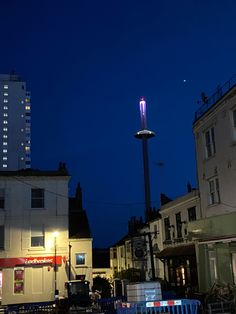 a city street at night with buildings in the background and a light tower lit up