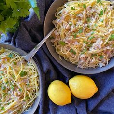 two bowls of pasta with lemons and parsley next to it on a blue towel