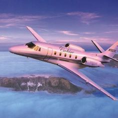 an airplane is flying over the clouds in the sky above some mountains and water at sunset