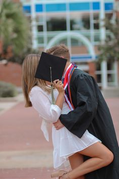 a young man and woman kissing each other in front of a building with a graduate's cap on