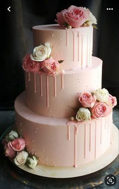 a three tiered cake with pink icing and flowers on it's side