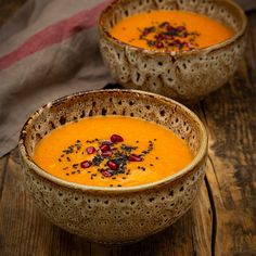 two bowls filled with soup on top of a wooden table