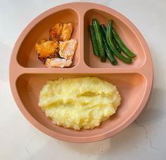 a pink plate with mashed potatoes, green beans and meat on it is shown