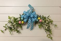 a blue bow hanging on the side of a white wall with flowers and greenery