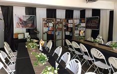 tables and chairs set up for an event with black table cloths, white folding chairs, and flowers