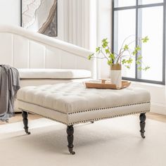 a living room with white furniture and a plant on the footstool in front of a window