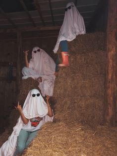 three people dressed in white are sitting on hay bales