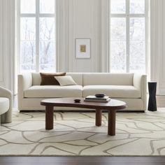 a living room with two couches and a coffee table in front of three windows