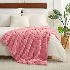 a bed with a pink blanket on top of it next to a potted plant