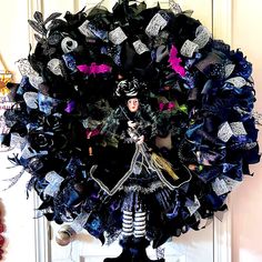 a black wreath with purple and blue decorations on the front door is adorned with a doll