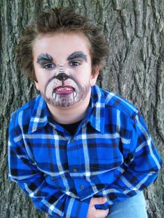 a young boy with his face painted to look like a bear is sitting in front of a tree