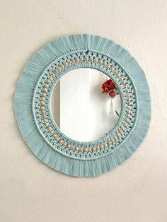 a round mirror hanging on the side of a wall with a red flower in it