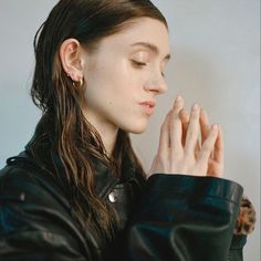 a woman with long hair wearing a black leather jacket and holding her hands to her face