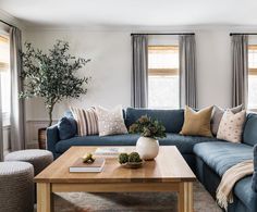 a living room with blue couches and pillows on the coffee table in front of two windows