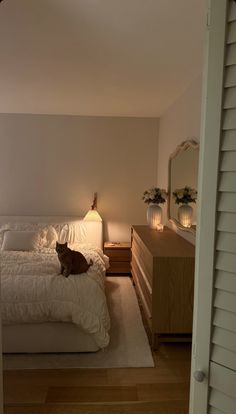 a cat sitting on top of a white bed in a bedroom next to a dresser